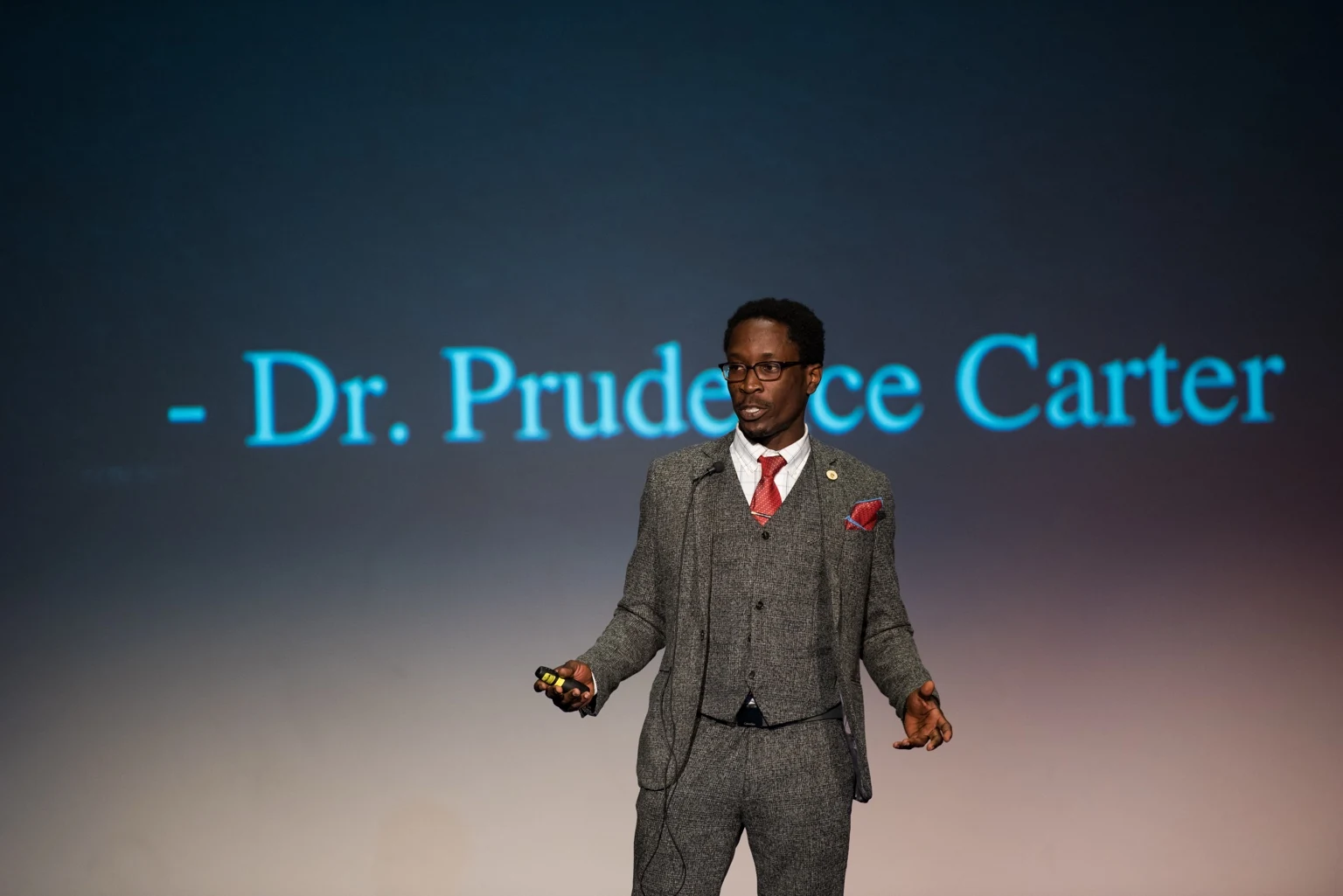 Rick Tamno presenting on stage with a Dr. Prudence Carter quotation behind him