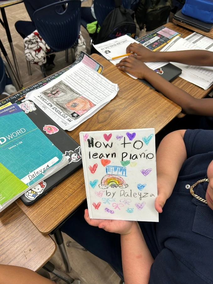 A child proudly displaying a handmade book titled How to Learn Piano